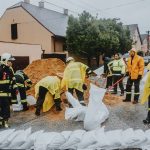 Equipe de emergência enche sacos de areia sob chuva para conter alagamentos em uma rua.