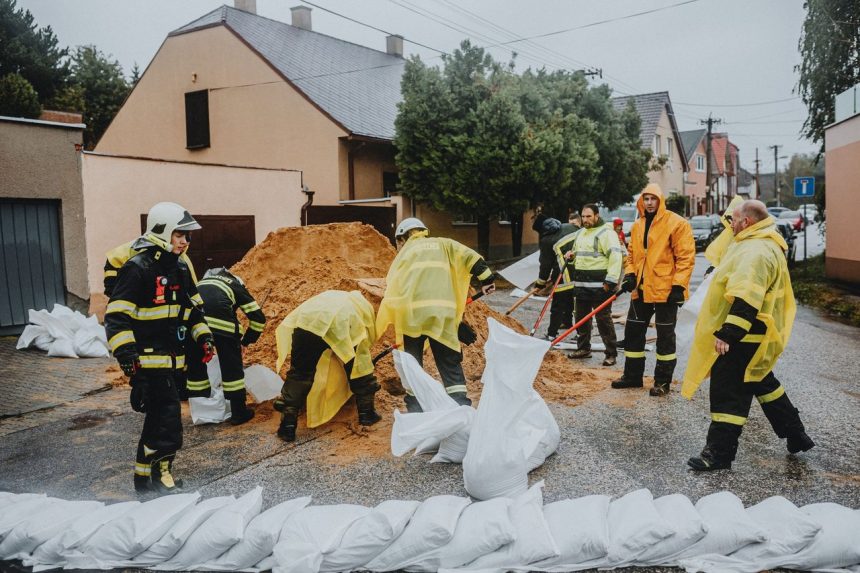 Equipe de emergência enche sacos de areia sob chuva para conter alagamentos em uma rua.
